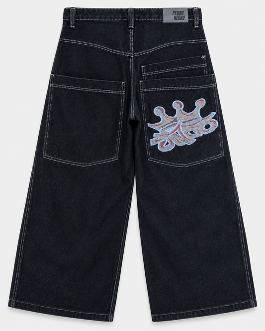 Pantalón baggy Perro Negro de mezclilla oscura, vista trasera, costuras contrastantes y bordado de corona JNCO gris con azul y rojo.